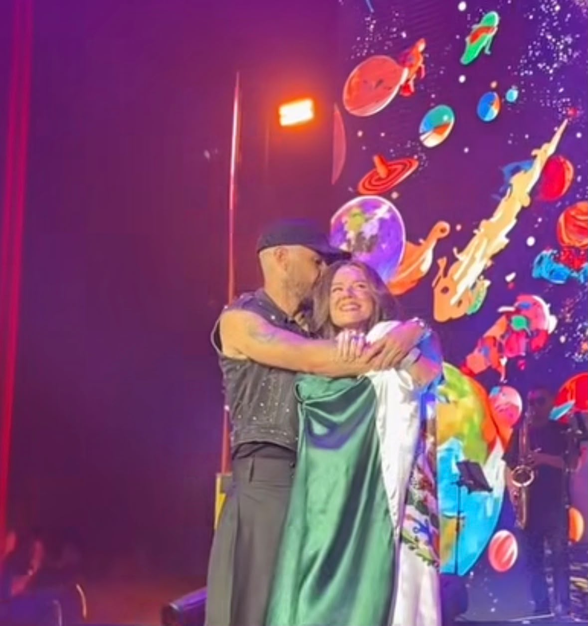 Jesse Huerta abraça e beija a cabeça da irmã Joy durante show de Jesse & Joy no Auditório Nacional, na Cidade do México, em 21 de outubro de 2026. A cantora permanece voltada ao público, sem retribuir visivelmente o abraço.